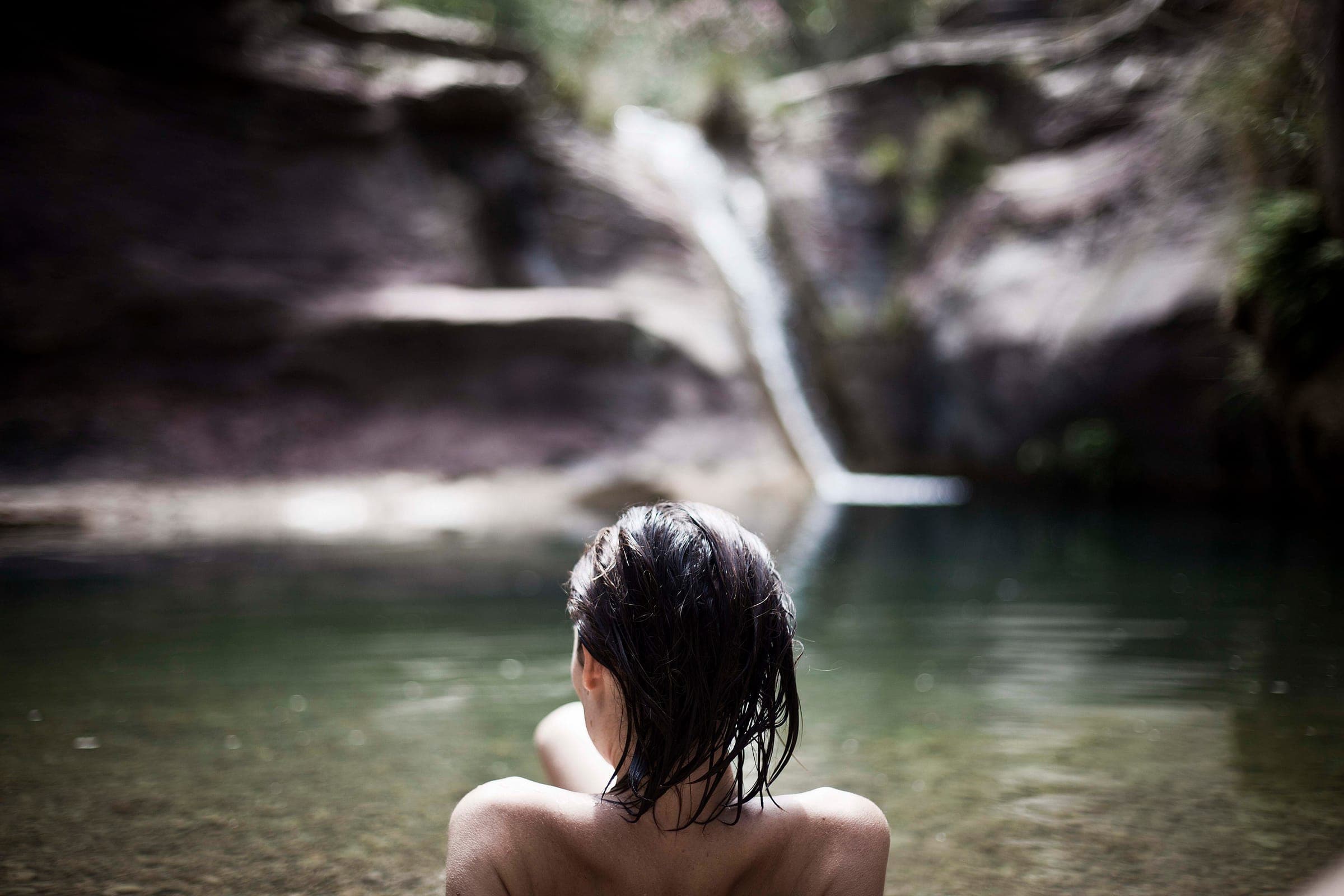 Una persona de espaldas, metida en el agua del Pozo Negro, mirando la cascada