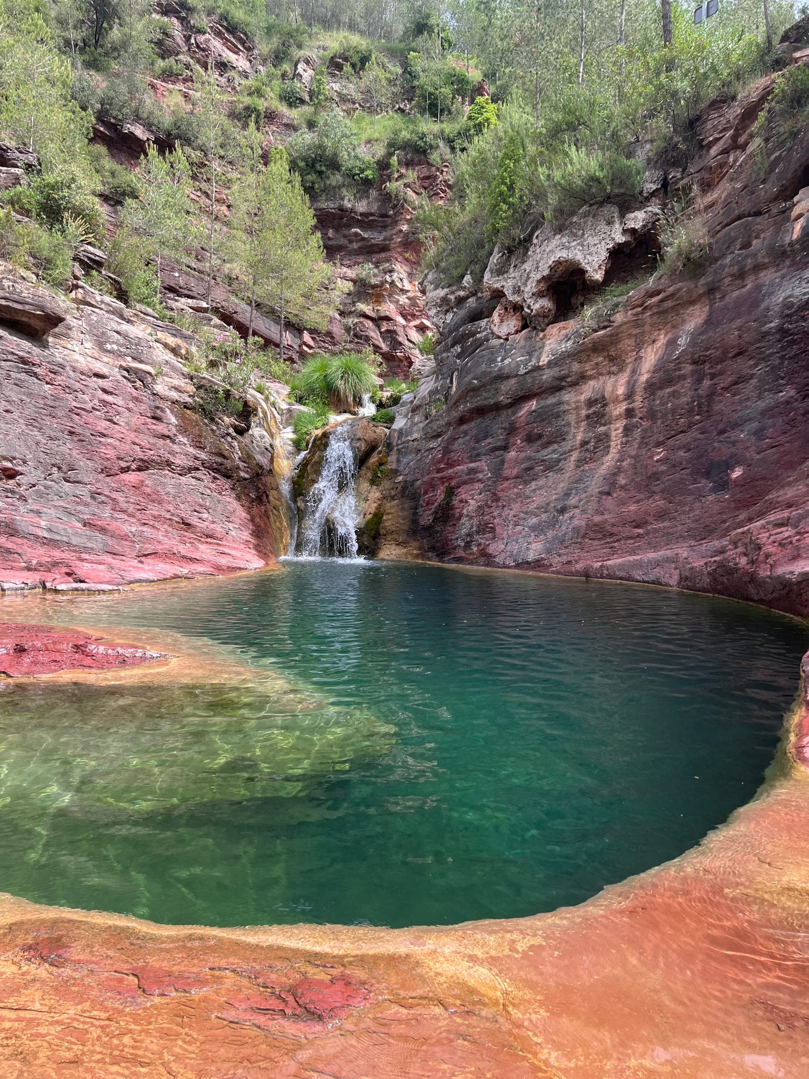 El Pozo Negro: poza de agua turquesa sobre roca roja con una pequeña cascada, en Fuentes de Ayódar